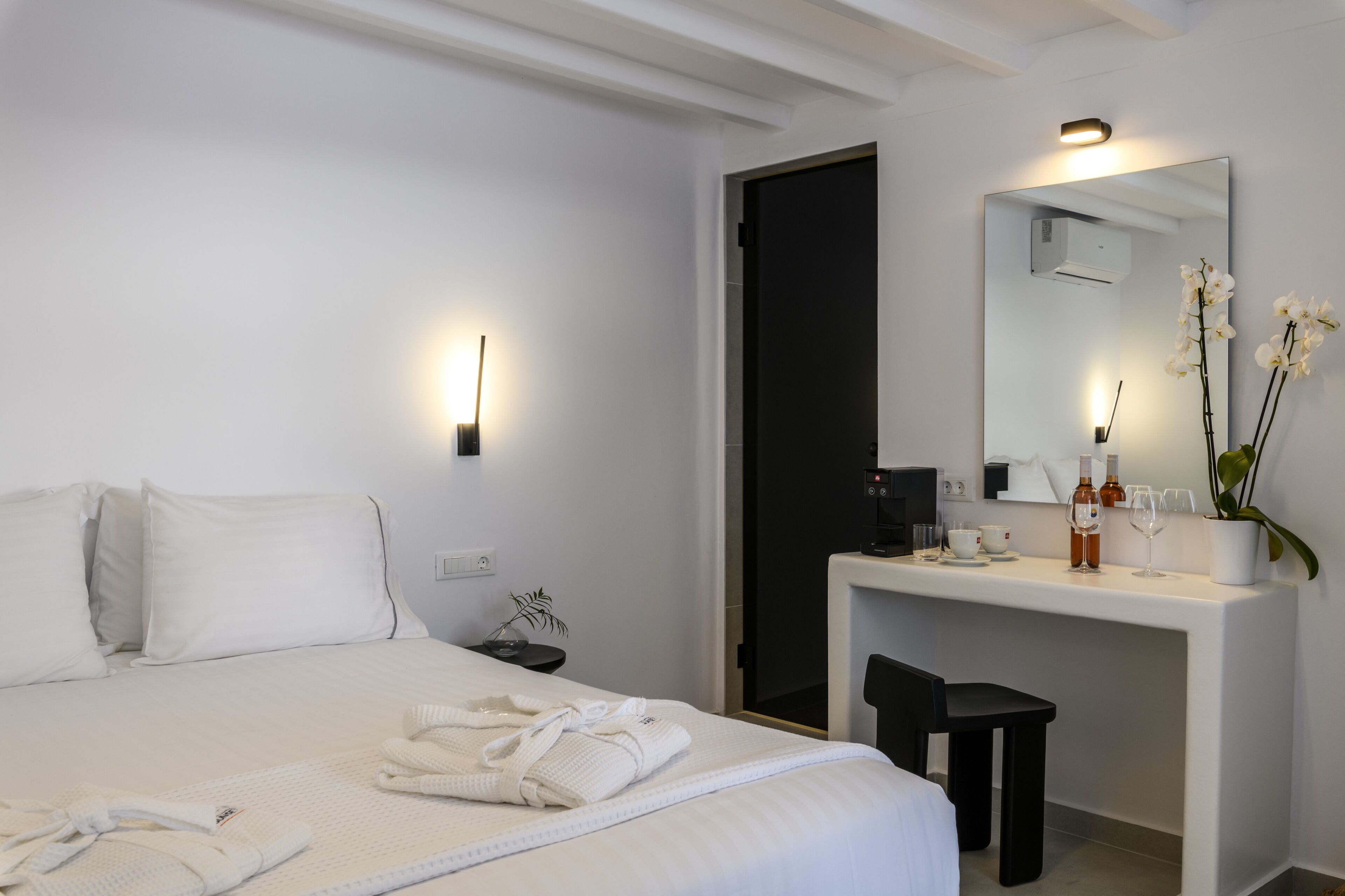 A hotel room with a bed, a desk, a mirror, and a small plant.