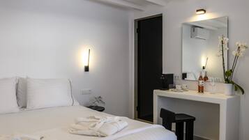 A hotel room with a bed, a desk, a mirror, and a small plant.