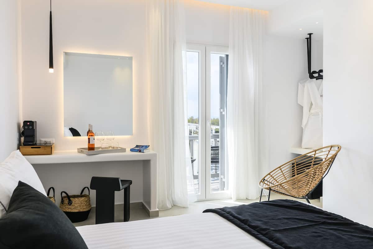 A modern hotel room with a bed, a desk with a computer, a chair, and a view of the outside.