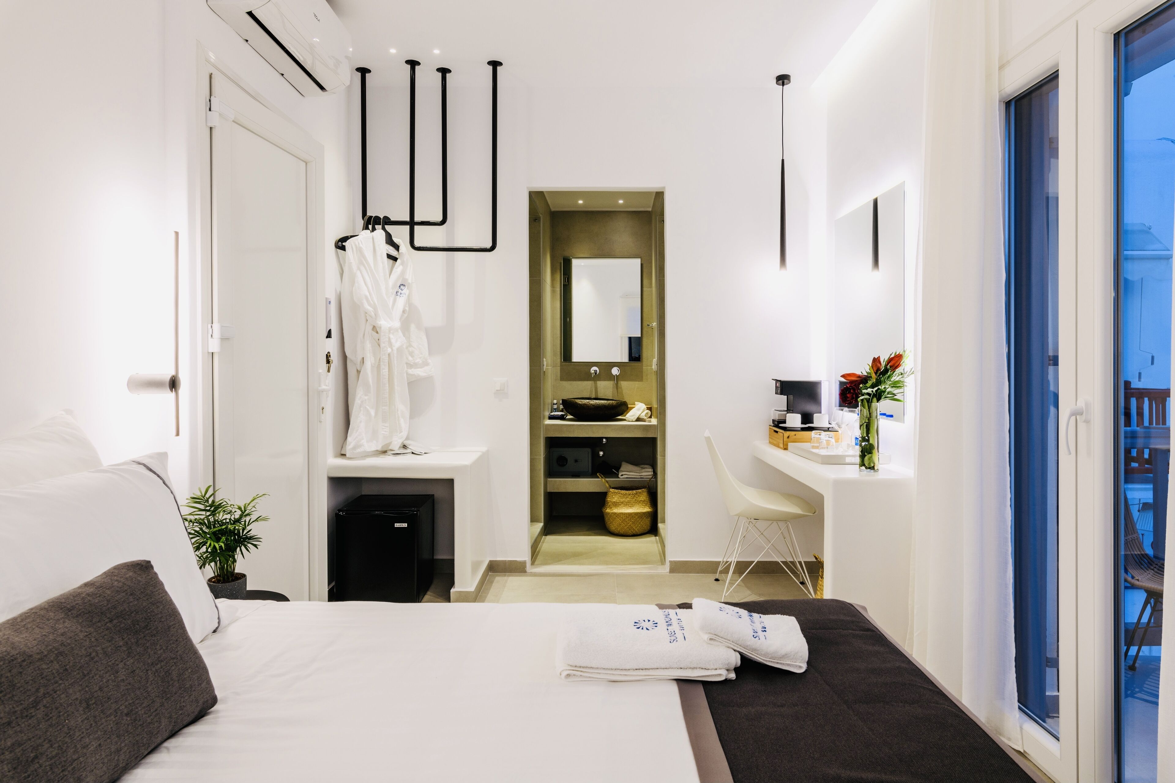 A modern hotel room with a bed, a desk, a bathroom, and a view of the outside.