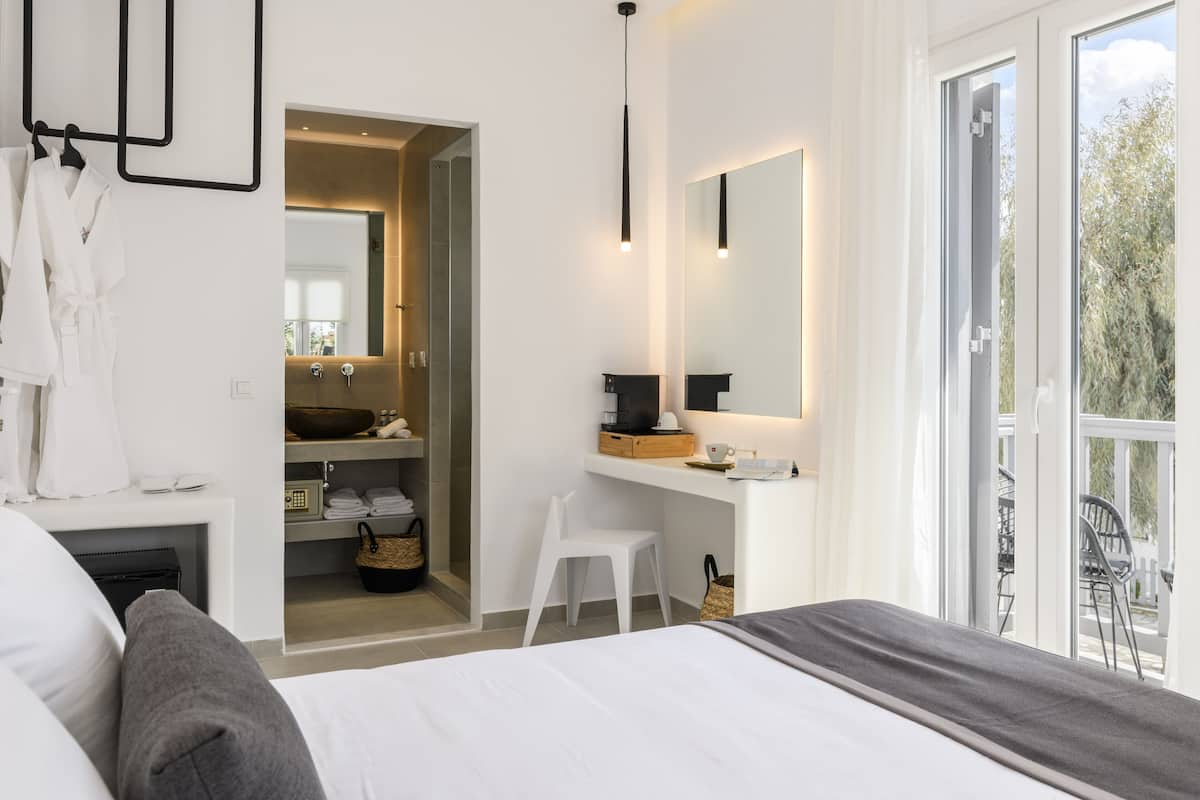 A modern bedroom with a large bed, a small desk, a mirror, and a view of the outdoors.