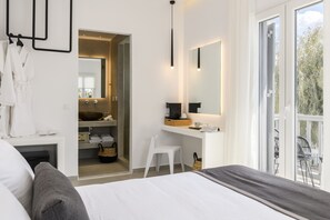 A modern bedroom with a large bed, a small desk, a mirror, and a view of the outdoors. - Sunset Windmills Suites (Mykonos)