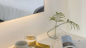 A hotel room with a bed, a bedside table with a glass of water, a cup, a tray, a book, and a potted plant.
