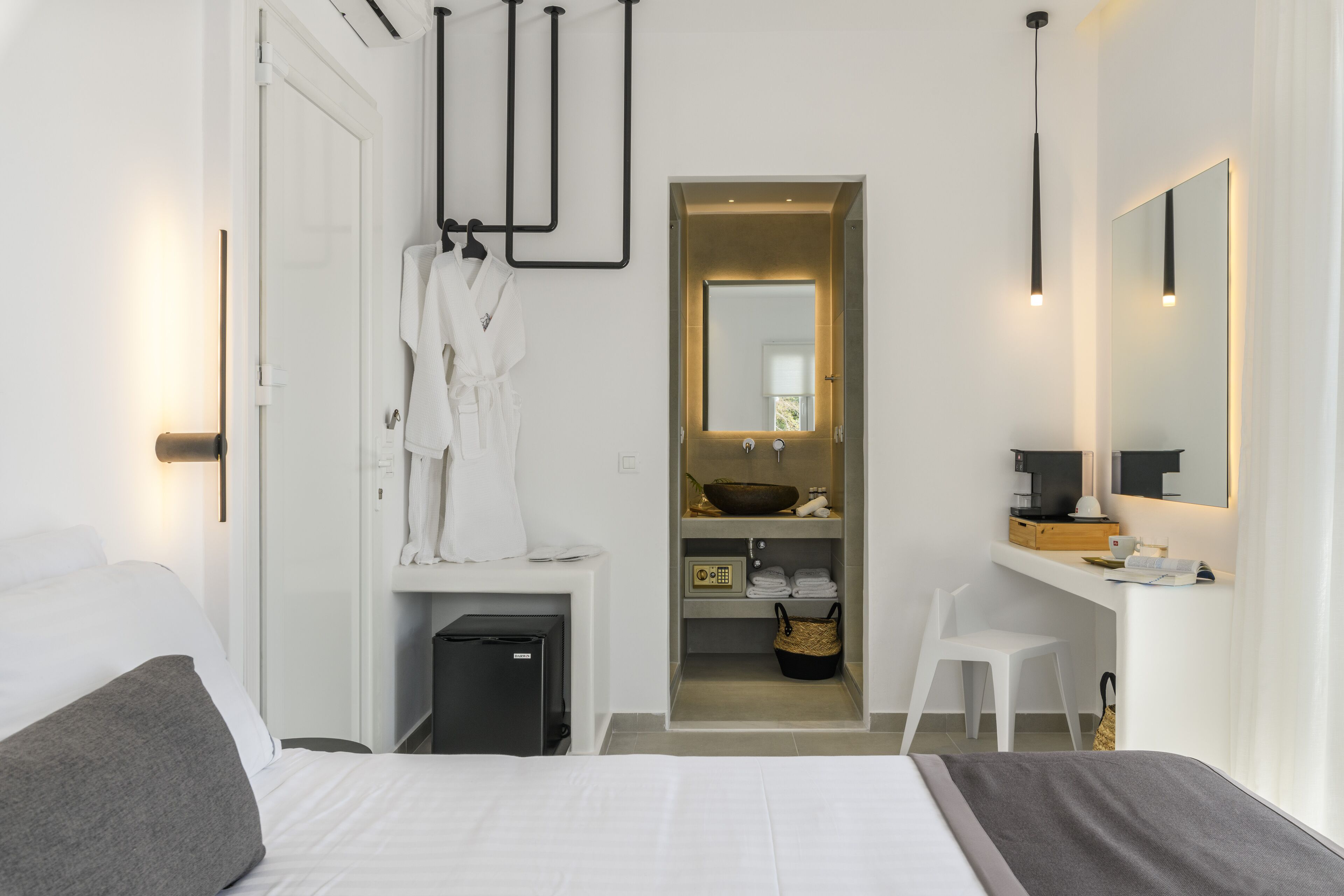A modern hotel room with a bed, a desk, a mirror, and a bathroom visible through an open door.