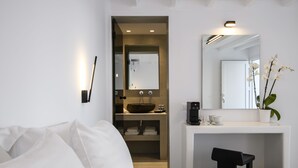 A modern hotel room with a large bed, a small desk with a sink, a mirror, and a potted orchid. - Sunset Windmills Suites (Mykonos)