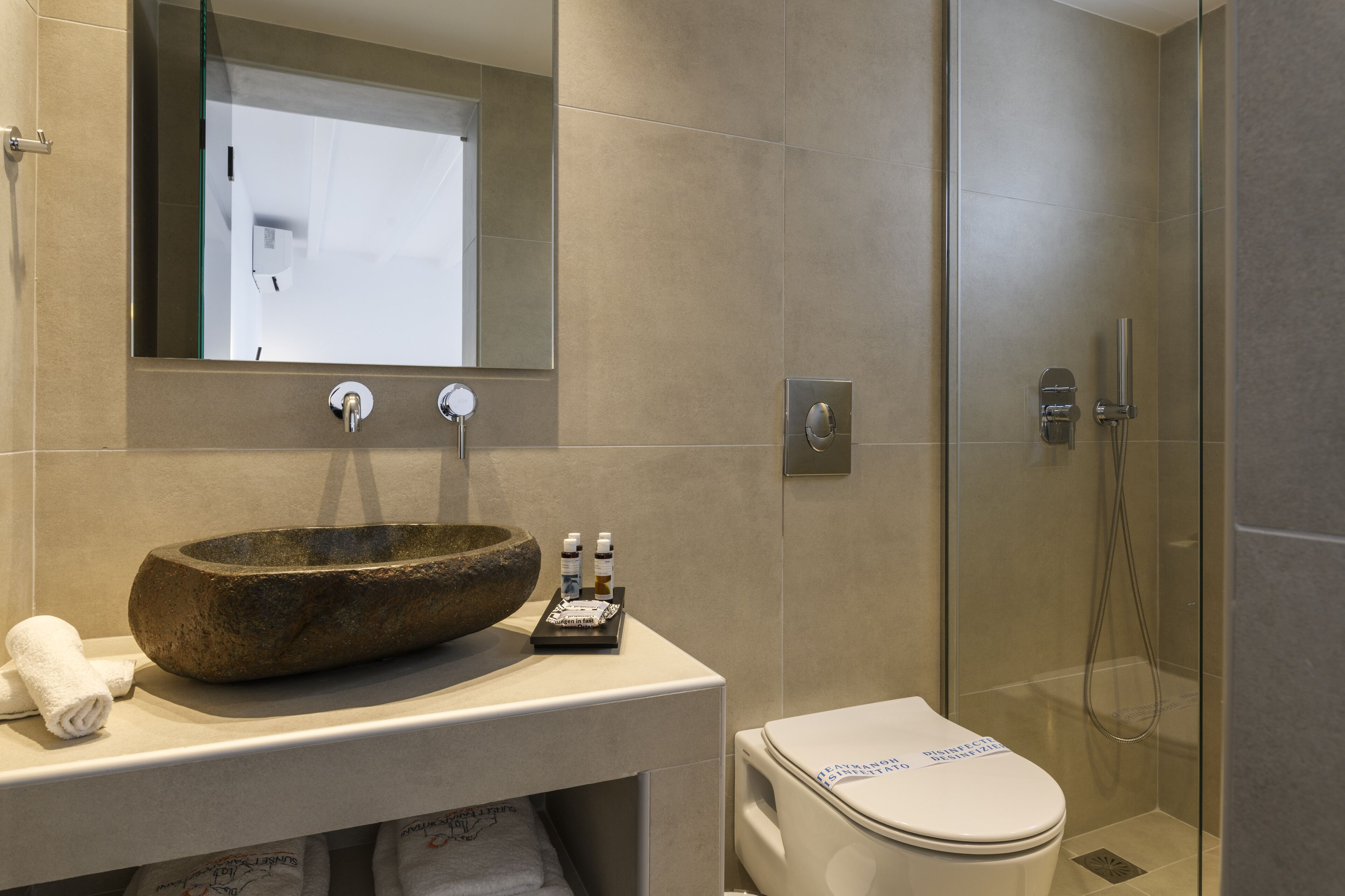 Un baño moderno con un lavabo de piedra, un inodoro y una ducha con mampara de vidrio.