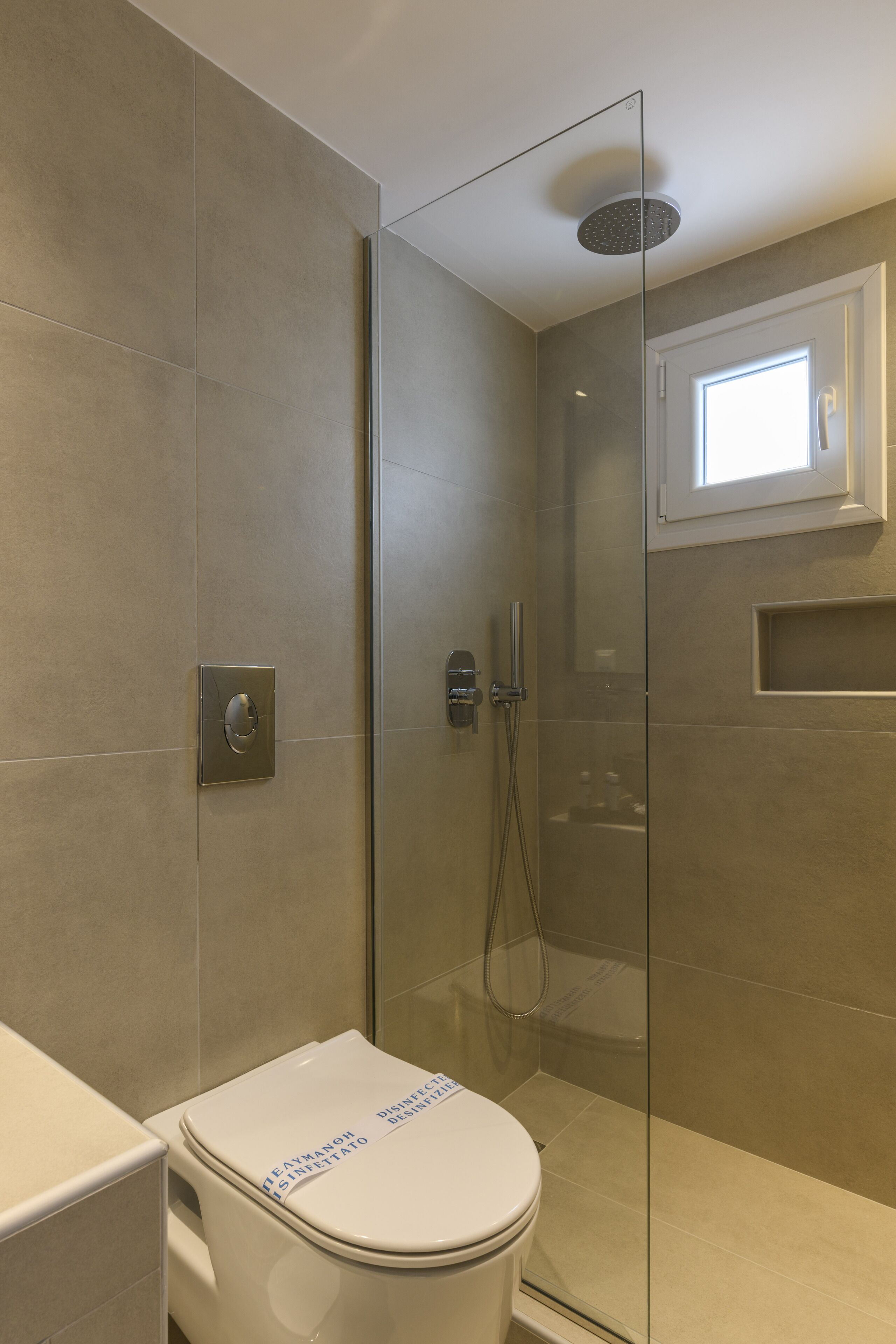 Un baño moderno con cabina de ducha de vidrio, inodoro con panel de control y ventana sobre la ducha.