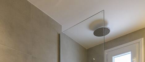 A modern bathroom with a glass shower enclosure, a toilet with a control panel, and a window above the shower.