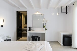 Una habitación de hotel moderna con cama, escritorio, espejo, taburete pequeño, cubo de basura y planta en maceta.