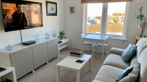 Ein modernes Wohnzimmer mit einer Couch, einem Couchtisch, einem Fernseher und einem Essbereich mit Stühlen und einem Tisch.