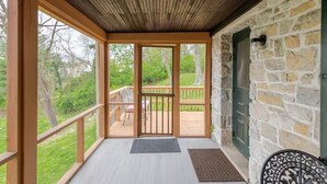 Un portico coperto con ringhiere in legno, un muro in pietra e vista su una zona verde.