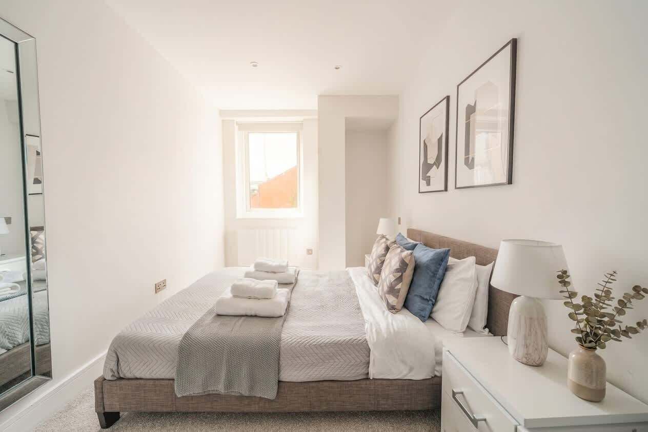 A bedroom with a bed, bedside table, lamp, and framed artwork.