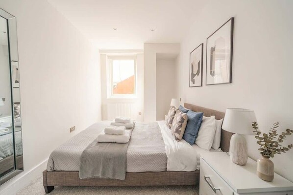 A bedroom with a bed, bedside table, lamp, and framed artwork.