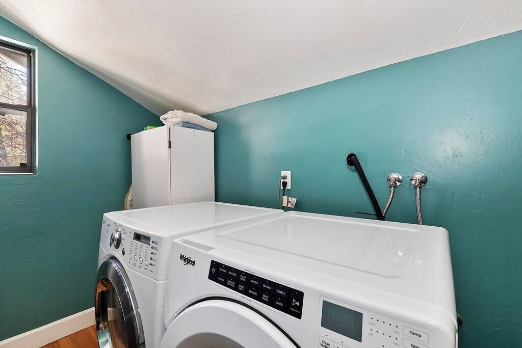 A laundry room with a Whirlpool washer and dryer, a white cabinet, and a window.