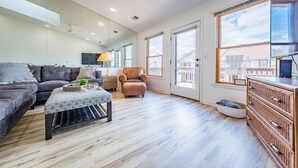 A spacious living room with a sectional sofa, a brown armchair, a coffee table, and a wooden dresser. - OCTIPI Your SenSEAS - Kitty Hawk, Sea Dunes, Open All Year, Flex Stays, Pool, Clubhouse (Kitty Hawk)