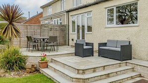 Un patio con mobiliario exterior, una valla de madera y una casa con techo de ladrillo.
