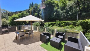 Een terras buiten met een barbecue, zitplaatsen en uitzicht op een bebost gebied.