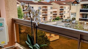 A balcony with a round table, a potted plant, and white orchids. In the background, there are multi-story buildings with balconies. - Champollion Appartment : A/C + Netflix + Garage (Albi)