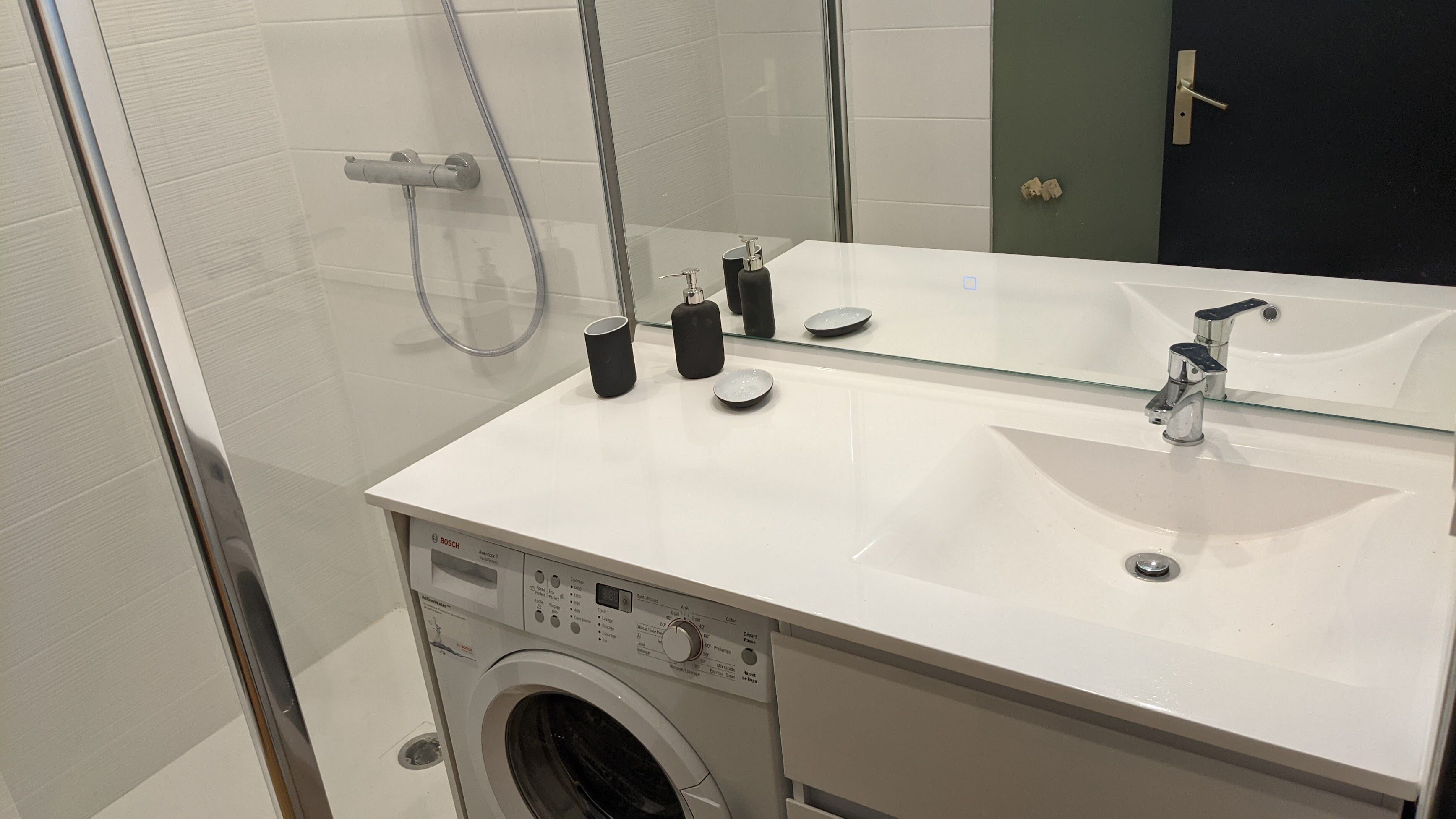 A bathroom with a white sink, a mirror, a washing machine, and a shower.