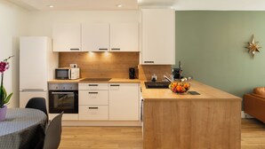 A modern kitchen with white cabinets, a wooden countertop, and a central island. There is a microwave, toaster, and sink on the countertop. A plant and a bowl of fruit are on the island. - Champollion Appartment : A/C + Netflix + Garage (Albi)