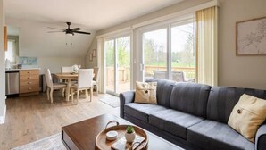 Ein großzügiges Wohnzimmer mit grauem Sofa, einem Esstisch mit Stühlen und einer Küchenzeile inklusive Kühlschrank und Schränken.