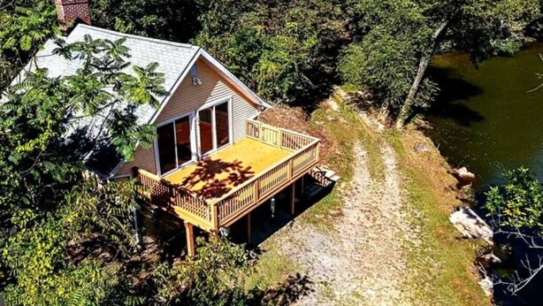 Ein Haus mit einer Terrasse mit Blick auf einen Fluss, umgeben von dichtem Wald.