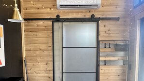 A modern kitchen with wooden walls, a black countertop, and a sliding door. - The Hemlock Tiny House (Logan)