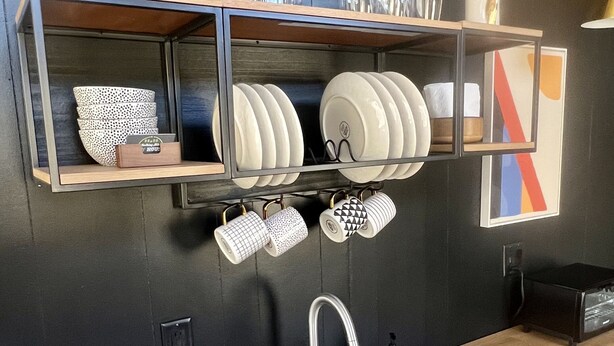 A kitchen with a stainless steel sink, wooden countertop, and shelves holding dishes and mugs. - The Hemlock Tiny House (Logan)