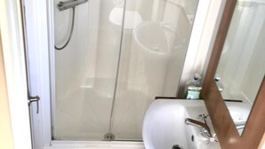 A bathroom with a glass shower enclosure, a white sink, and a mirror.