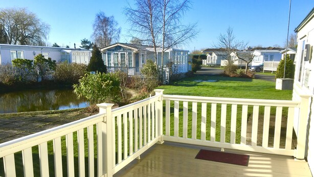A wooden deck with a white railing, a small table, and a bench.