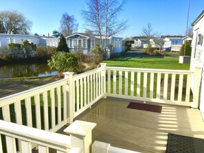 Eine Holzterrasse mit weißer Brüstung, einem kleinen Tisch und einer Bank.
