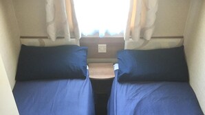 A compact RV interior with two beds, a small table, and curtains.
