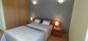 A bedroom with a bed, two bedside tables, a nightstand, and a wooden wardrobe.