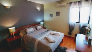Une chambre d’hôtel avec un lit, des lampes de chevet, un bureau et une fenêtre avec des rideaux.