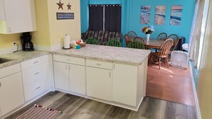 A kitchen with white cabinets, a coffee maker, and a dining area with a table and chairs.