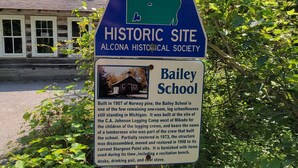 A sign for Alcona County Historic Site, mentioning Bailey School built in 1907 of Norway pine, one of the few remaining one-room log schoolhouses still standing in Michigan.