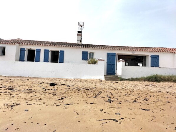 Un bâtiment situé sur la côte, doté d’un toit recouvert de tuiles, de murs blancs et de volets bleus.
