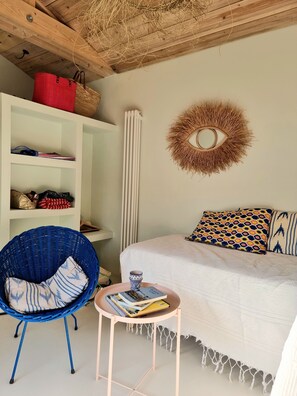 Une pièce confortable avec un lit, un fauteuil bleu, une petite table avec un livre, une armoire blanche et un élément décoratif mural.