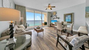 A spacious living room with a large window overlooking the sea, a ceiling fan, and a dining area with chairs and a table. - ⛱️Great Views-5 Pools-Majestic Beach Towers 1-1911⛱️ (Panama City Beach)