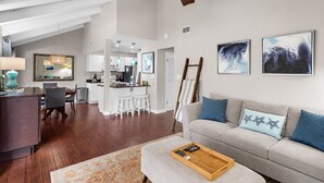 A modern living room with a sofa, a coffee table, a dining area with chairs, and a kitchen in the background. - ✨Walk2Beach-Renovated-Pools-Large Balcony- Pet Friendly-Sweet Magnolia✨ (Miramar Beach)