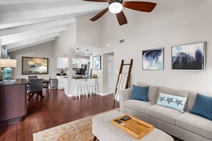A modern living room with a sofa, a coffee table, a dining area with chairs, and a kitchen in the background.
