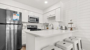 A modern kitchen with white cabinetry, stainless steel appliances, and a central island with bar stools.