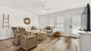 A modern living room with a white ceiling, two sofas, wicker chairs, a round coffee table, and a ceiling fan.