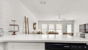 A modern kitchen with white cabinetry, a dishwasher, and a dining area with a sofa and wicker furniture.