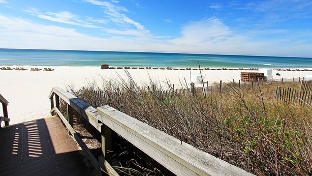 A beach with a wooden boardwalk leading to the shore, a sandy beach, and a clear blue sky.