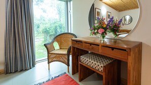 A room with a wooden desk, a wicker chair, a mirror, and a window with curtains.