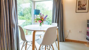 A dining area with a round table and four chairs, a vase of flowers, and a lamp.