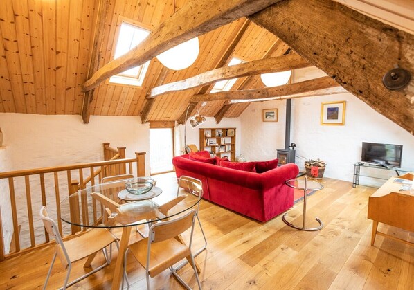 Une pièce en bois aux hauts plafonds, avec un canapé rouge, une table à manger en verre et un téléviseur.