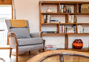 Un salon chaleureux avec un fauteuil gris, une bibliothèque en bois remplie de livres et un vase décoratif.