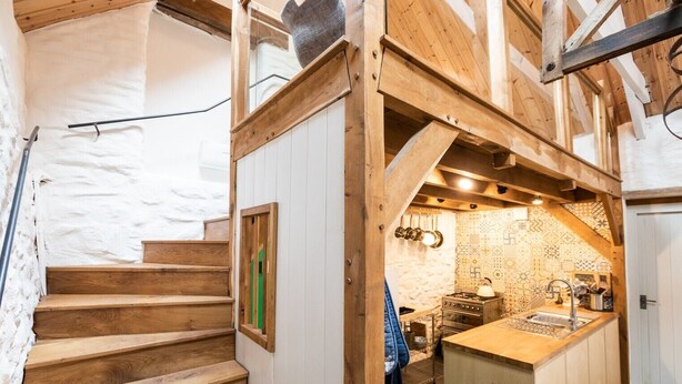 Una escalera de madera conduce a una zona de cocina con estufa y lavamanos.